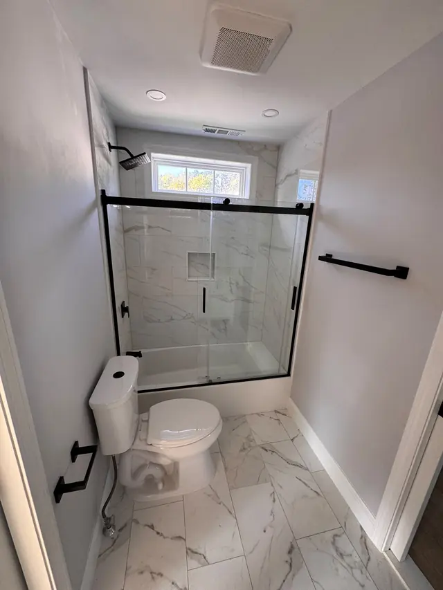 Bathroom view showing a bathtub, glass enclosure, toilet, and tiled floor.