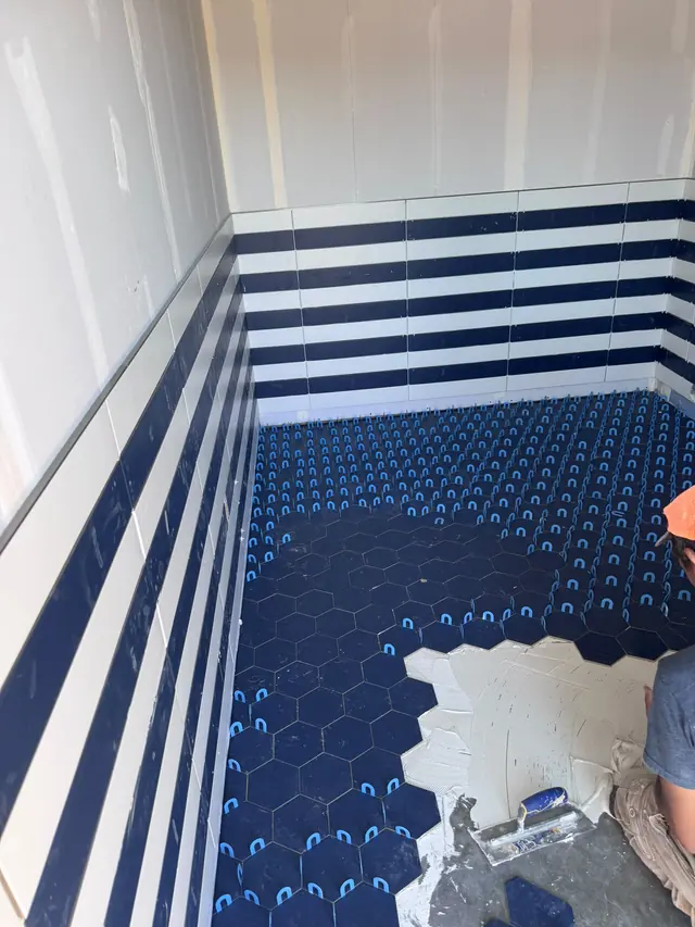 Blue bathroom floor tiles being installed below striped wall tile.