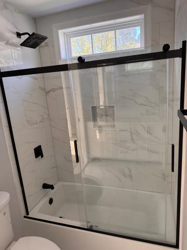 A bathtub with a glass shower enclosure and tiled walls.