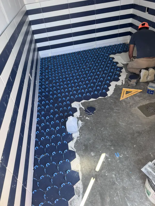 A worker installing blue bathroom floor tile during the project.